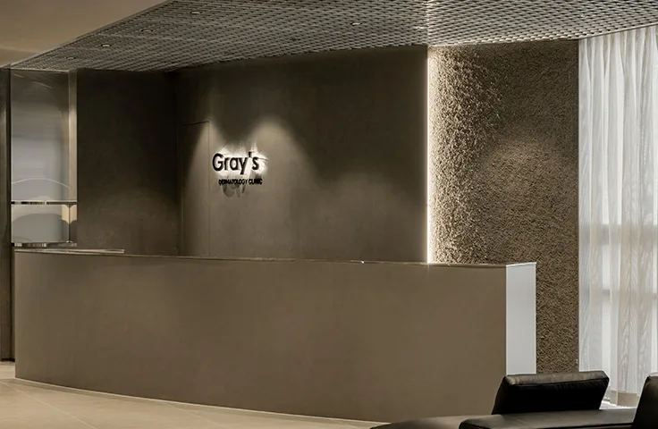 Reception desk at Gray's Dermatology Clinic, showing the Gray's DERMATOLOGY CLINIC logo on a dark gray wall