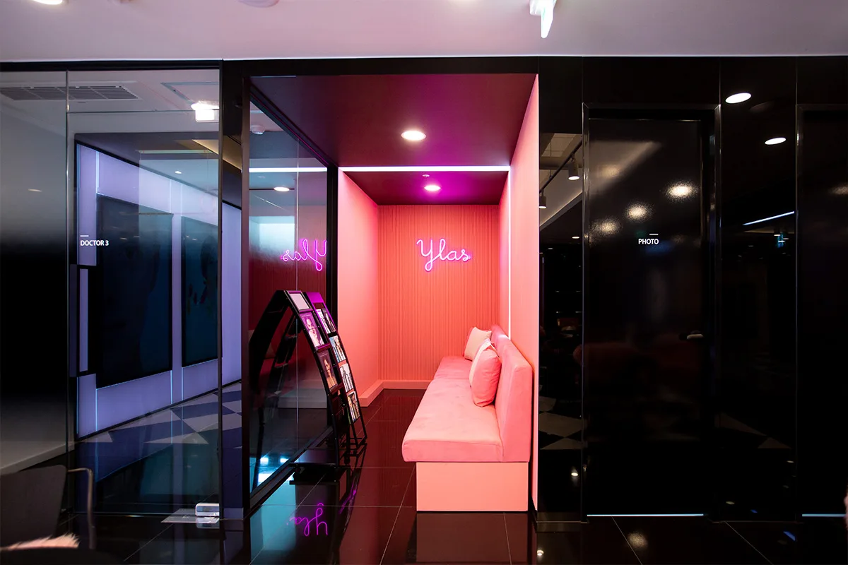 Waiting area at Ilas Clinic, showing a bench in front of a pink wall with a lit Ylas neon sign