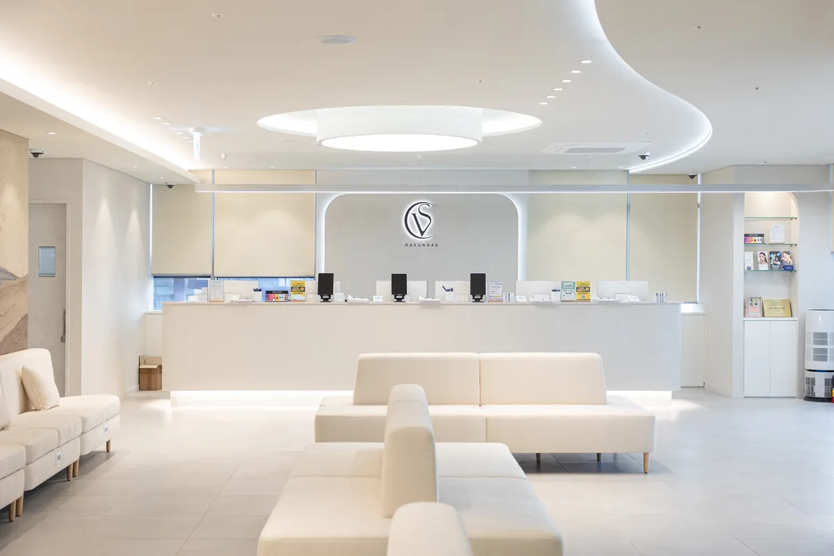 Reception area at Vance Clinic Haeundae, showing a white sofa and a reception desk with a V logo